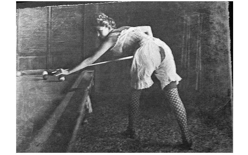 Black and white photograph of a prostitute in lingerie playing pool.